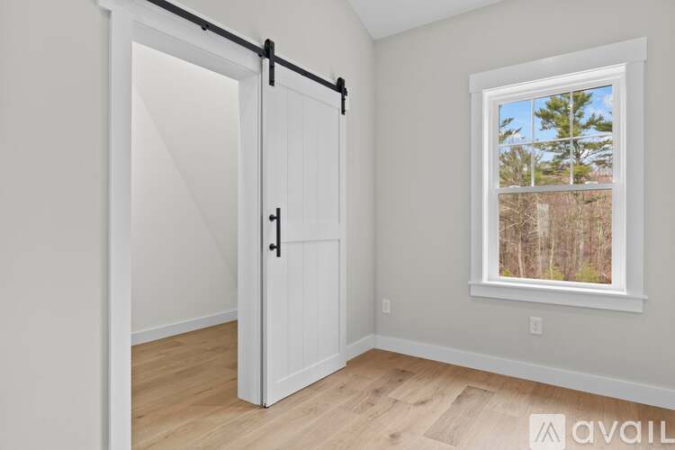A room with a white door and a window showing a view of trees.