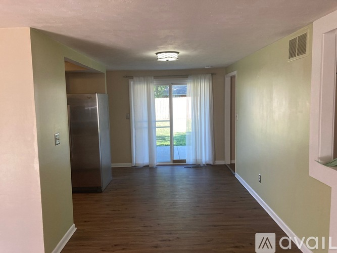 A spacious room with wooden floors and a large window with curtains.