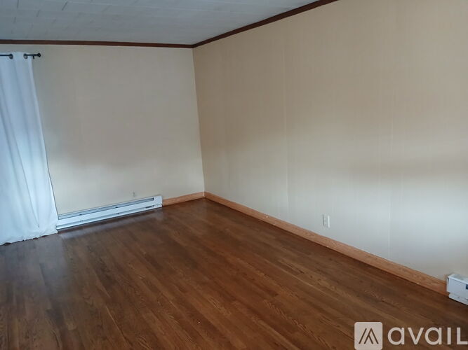 A room with wooden flooring and a window with white curtains.