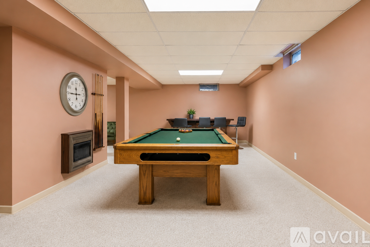 A pool table is in the middle of a room with a clock on the wall.