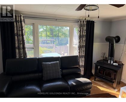 A black leather couch sits in a living room with a wood stove and a ceiling fan.