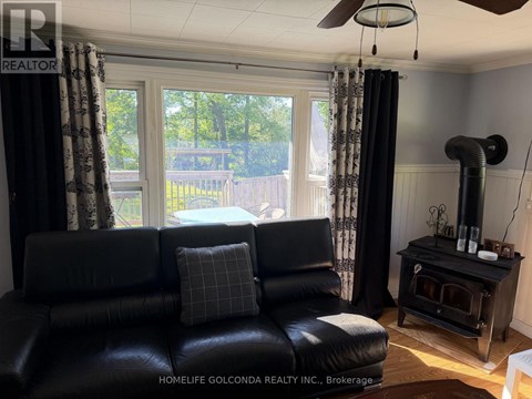 A black leather couch sits in a living room with a wood stove and a ceiling fan.