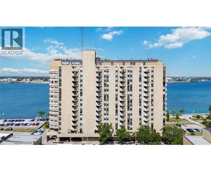 A tall building with a balcony on the top floor overlooks a body of water.