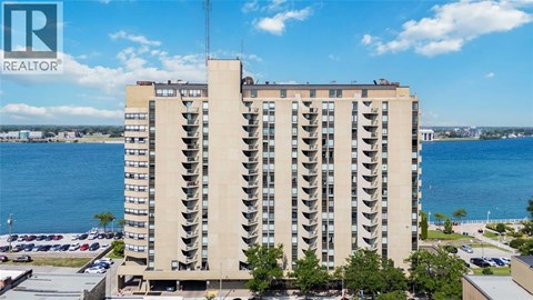 A tall building with a balcony on the top floor overlooks a body of water.