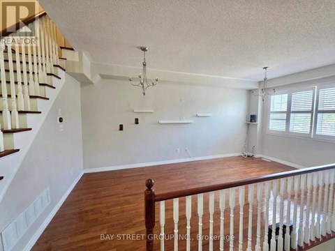 A spacious living room with a staircase on the left and a chandelier hanging from the ceiling.