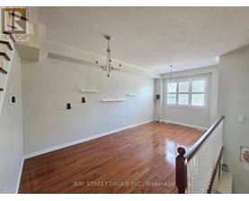 A spacious room with wooden floors and white walls, furnished with a chandelier and a window with blinds.