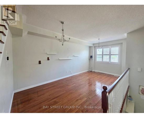 A spacious room with wooden floors and white walls, furnished with a chandelier and a window with blinds.