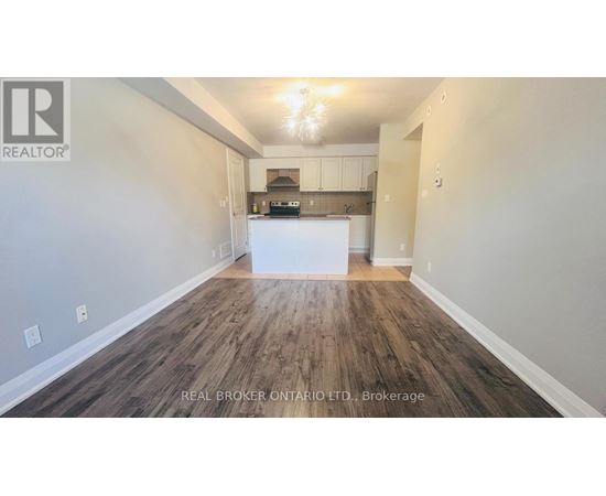 A spacious room with wood flooring and a kitchenette in the background.