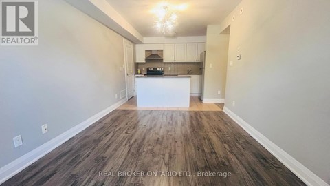 A spacious room with wood flooring and a kitchenette in the background.