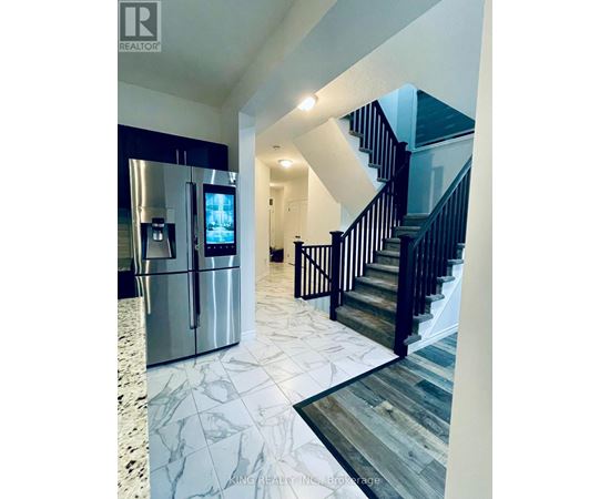 A modern kitchen with a refrigerator and stairs in the background.