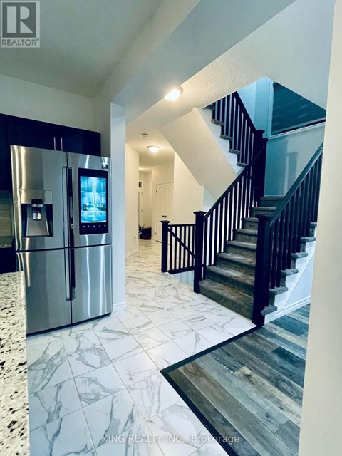 A modern kitchen with a refrigerator and stairs in the background.