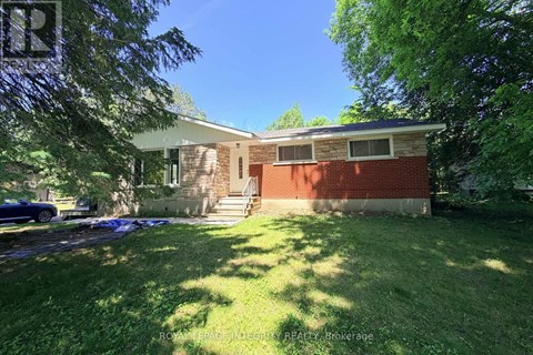 A house with a red brick wall and a white roof is surrounded by green grass and trees.