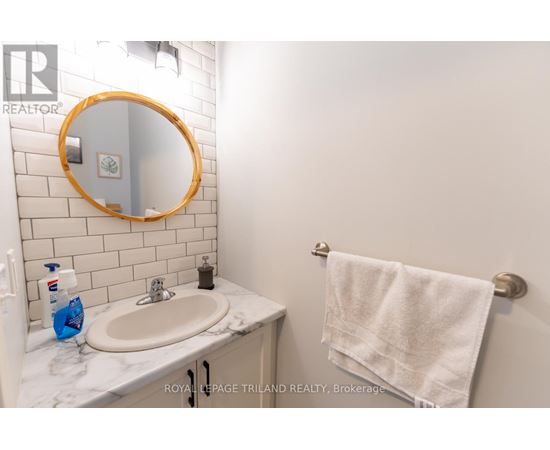 A white bathroom with a round mirror and a towel hanging on the towel rack.
