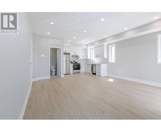 A spacious, empty room with light wood flooring and white walls.