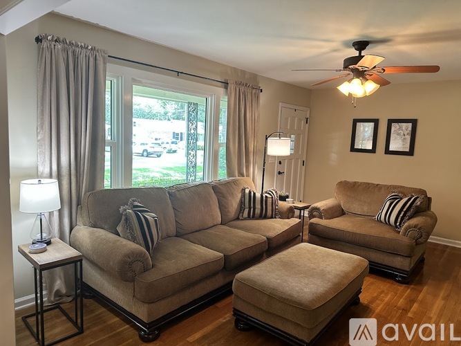 A living room with a large sectional sofa and a smaller loveseat, both with striped pillows, a side table with a lamp, and a ceiling fan.