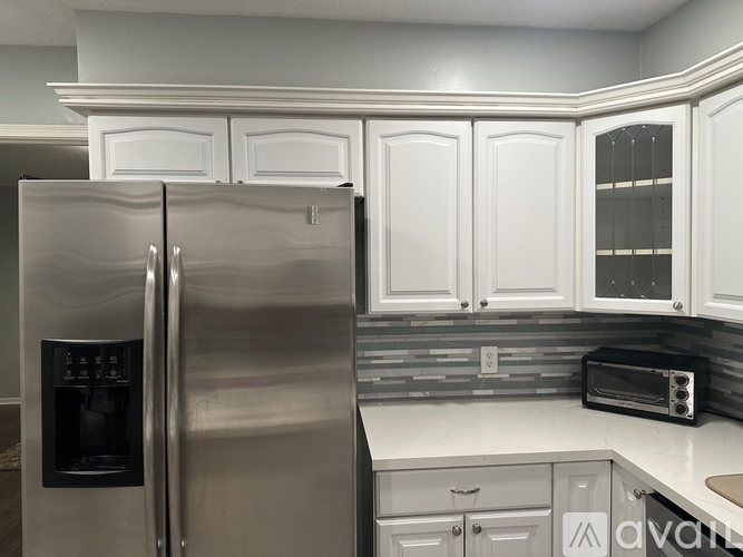 A stainless steel refrigerator with a digital display and ice maker sits in a kitchen with white cabinets.