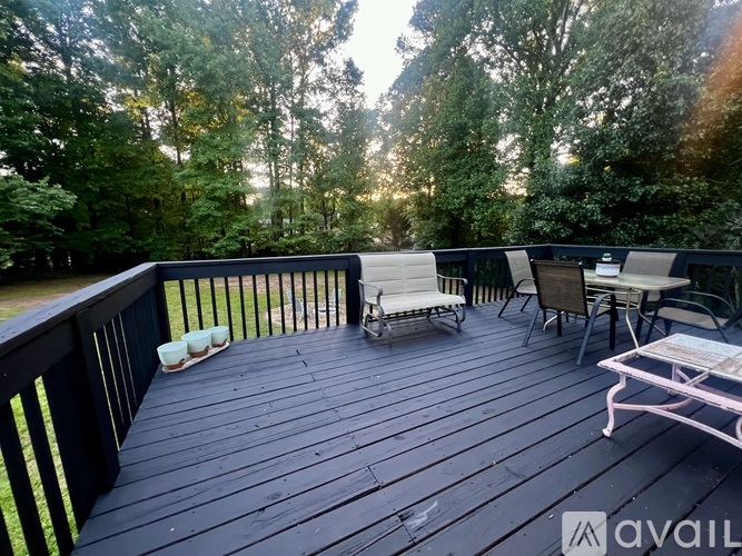 A wooden deck with chairs and a table surrounded by trees.