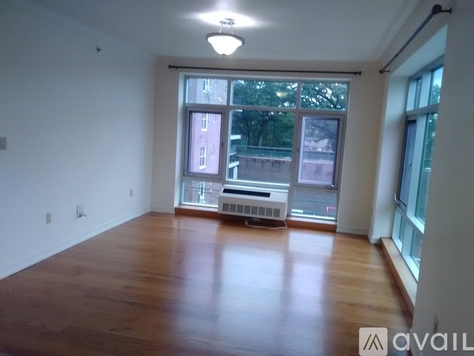 A spacious room with wooden floors and a large window overlooking a cityscape.