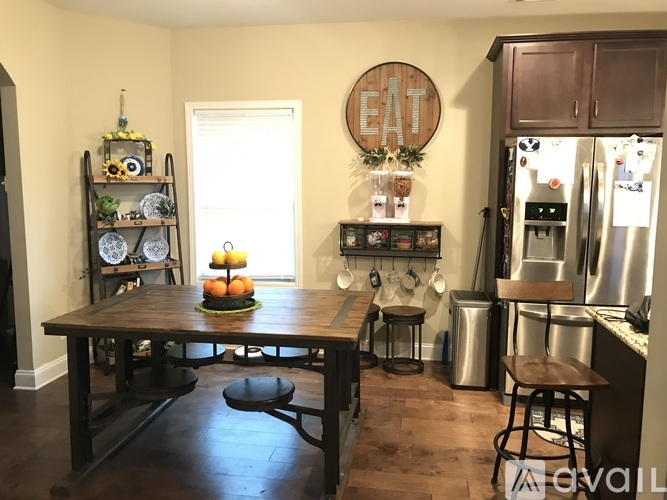 A kitchen with a wooden table and chairs, a hanging sign that says "EAT", and a shelf with various items.