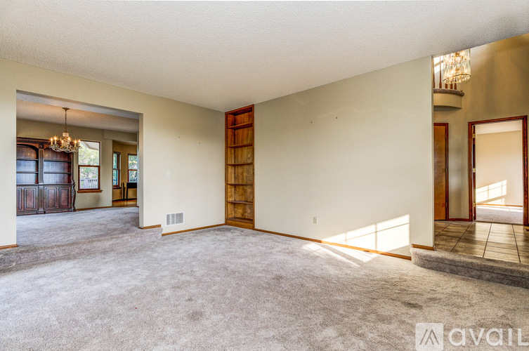 A spacious living room with a carpeted floor and a chandelier hanging from the ceiling.