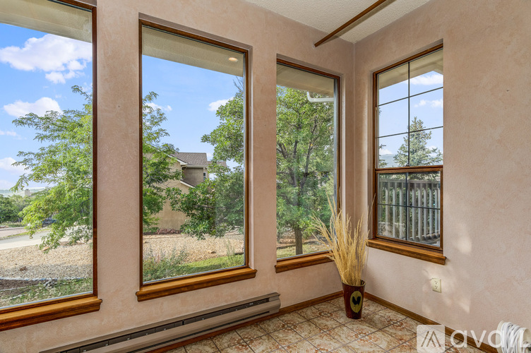 A room with three windows showing a view of a house and trees.