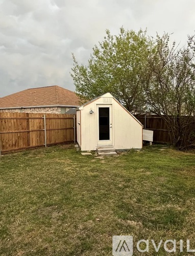 A small white shed with a door is situated in a grassy backyard.