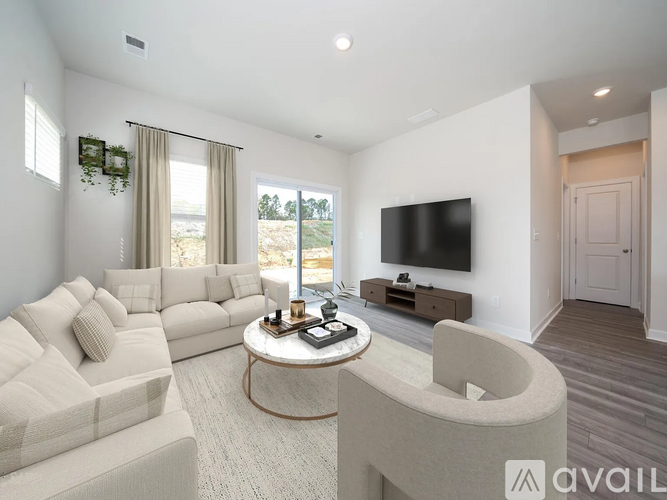 A living room with a white sofa, a round coffee table, and a flat-screen TV mounted on the wall.