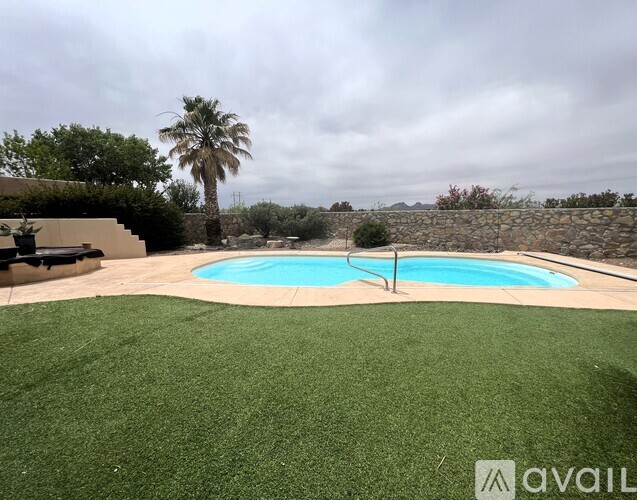 A pool surrounded by a green lawn and a stone wall.