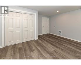 A room with wooden flooring and white walls, with a door on the right and a white door with a window on the left.