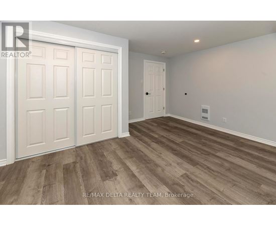 A room with wooden flooring and white walls, with a door on the right and a white door with a window on the left.