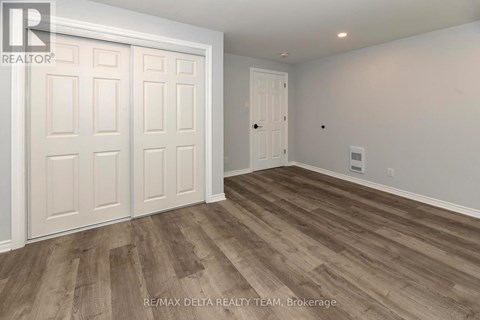 A room with wooden flooring and white walls, with a door on the right and a white door with a window on the left.