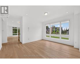 A spacious room with wooden flooring and a large window showing a view of a residential area.