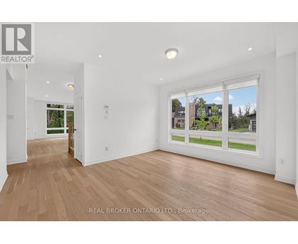 A spacious room with wooden flooring and a large window showing a view of a residential area.