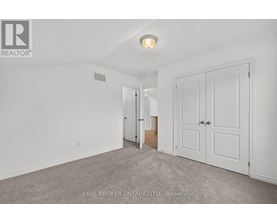 A white bedroom with a carpet floor and a Real Broker logo.