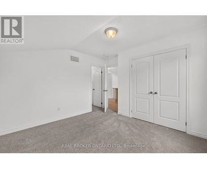 A white bedroom with a carpet floor and a Real Broker logo.