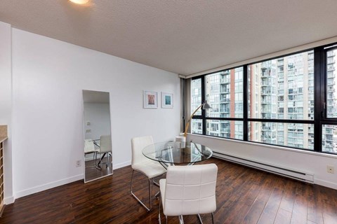 A white chair is in front of a glass table in a room with a view of apartment buildings.