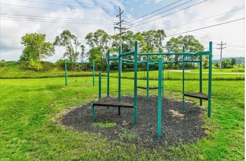 A playground with a green swing set in the middle of a grassy area.