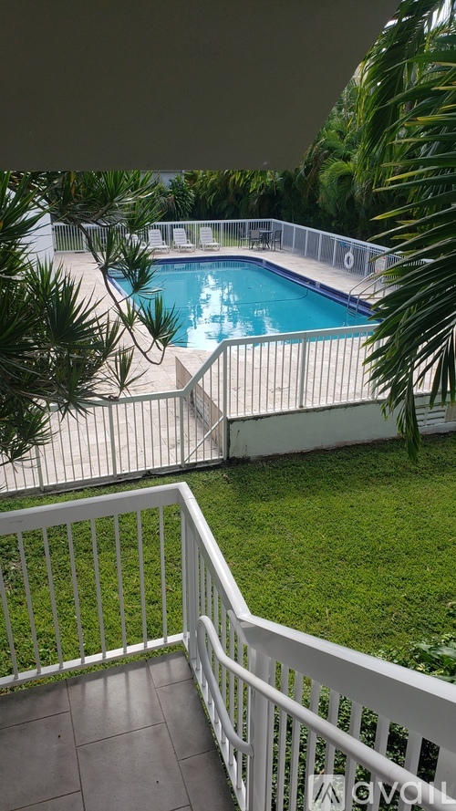 A pool surrounded by a white fence and greenery.