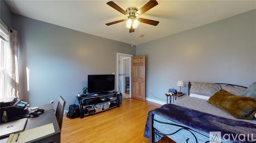A bedroom with a bed, a television, a chair, and a ceiling fan.
