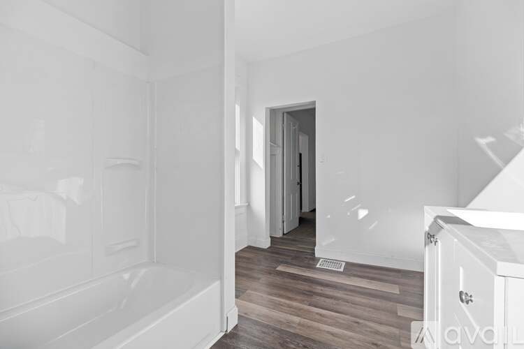 A white bathroom with a wooden floor and a white bathtub.