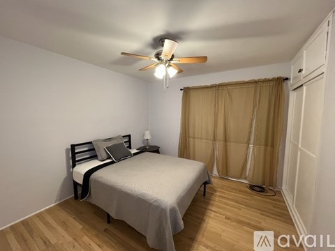 A bedroom with a bed, a ceiling fan, and a window with curtains.
