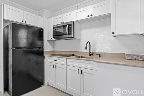 A black refrigerator is in a kitchen with white cabinets.