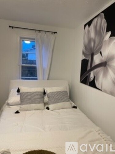 A bedroom with a white bed and a large white flower picture on the wall.