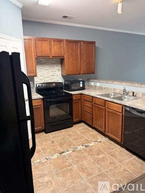 A kitchen with a black refrigerator, black oven, and brown cabinets.