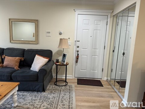 A living room with a grey couch and a small table with a lamp on it.