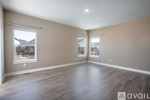 A spacious room with wooden flooring and two windows.