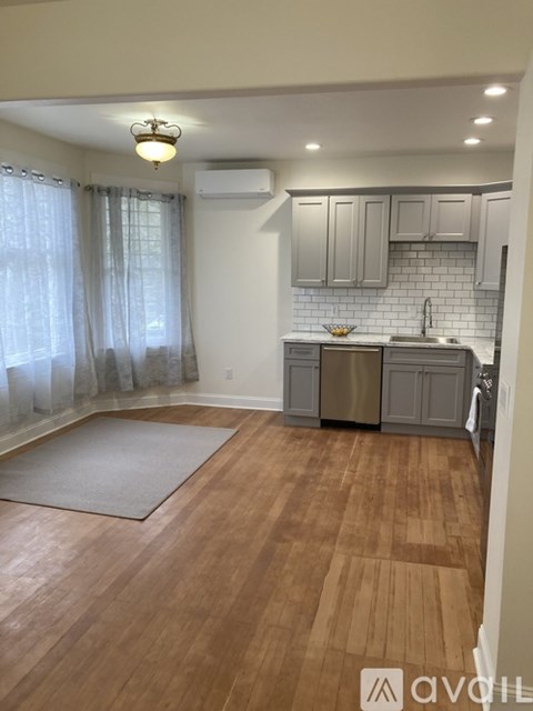 A kitchen with wooden floors and a grey rug in the middle.