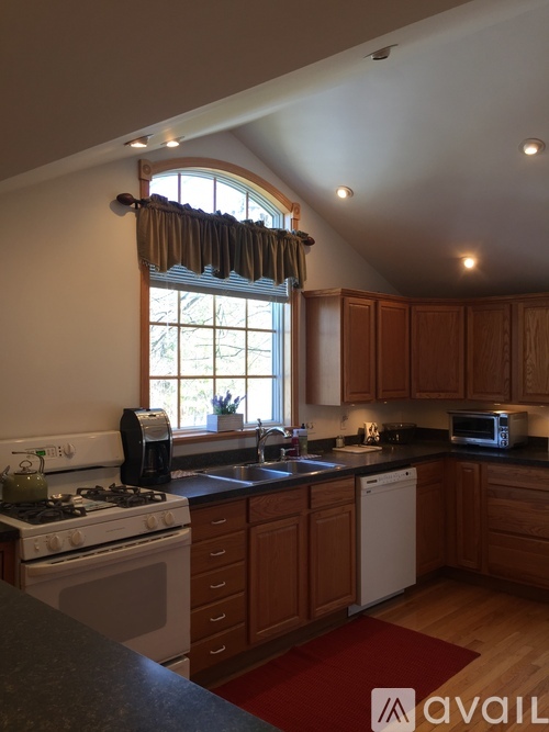 A kitchen with wooden cabinets and a window with curtains.