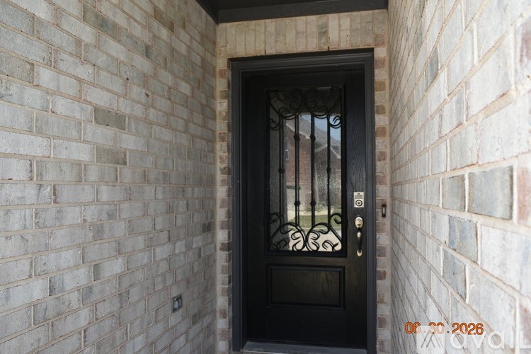 A black door with a metal grill is set in a brick wall.