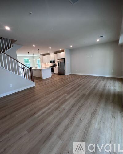 A spacious room with wooden flooring and a staircase on the left side.